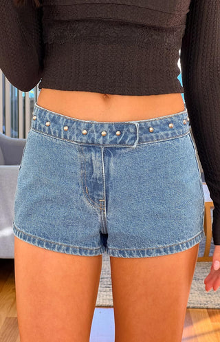Pantalones cortos vaqueros Mollie de mezclilla de lavado medio y talle bajo con tachuelas.